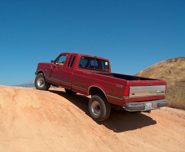 Red 1989 Ford F-250 pickup truck, rear 3/4 view, driving on dirt