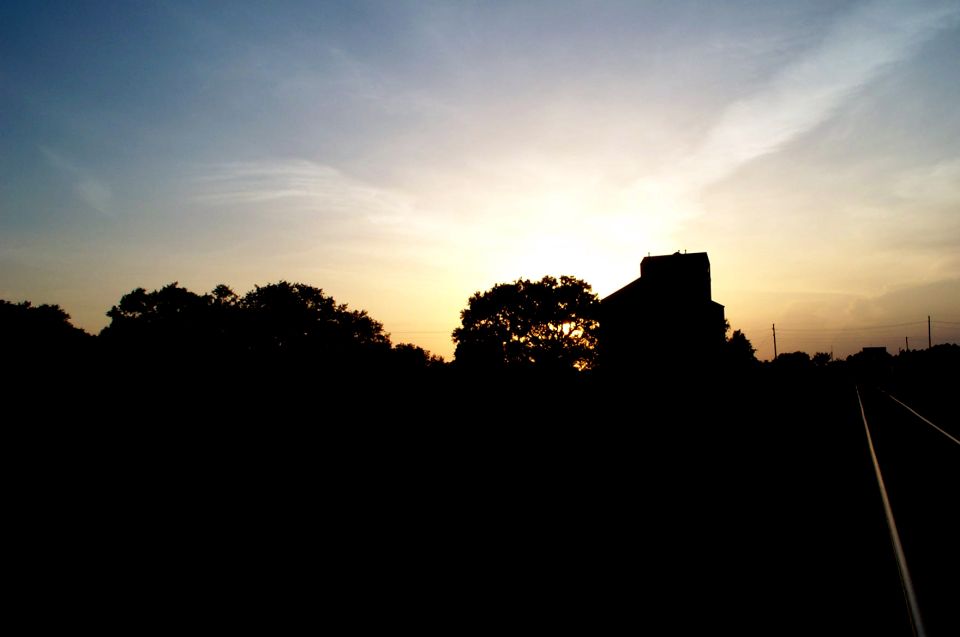 Sunset over railroad tracks with a silhouetted building and trees
