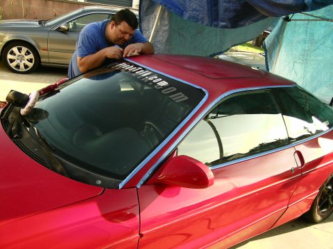 1993 Ford Probe - A man applies a banner to the windshield of a red 1993 Ford Probe while another car is parked behind it.