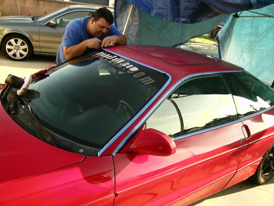 Red 1993 Ford Probe with blue tape on windshield and a man applying a banner