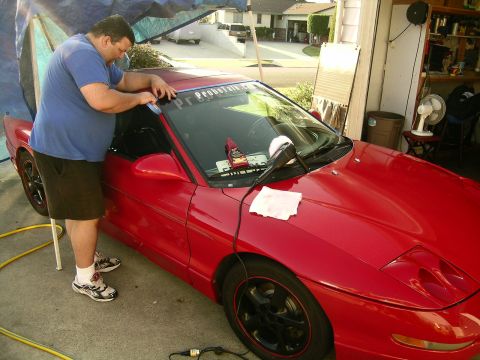 1993 Ford Probe - A man applies a sticker to the windshield of a red sports car.