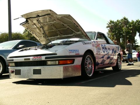 1993 Ford Probe - A white race car, possibly a Mazda MX-6, is parked with its hood open, displaying various racing decals and a checkered flag design.