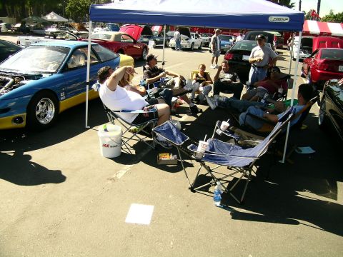 1993 Ford Probe - People relax under a tent at a car meet, with a 1993 Ford Probe prominently displayed.