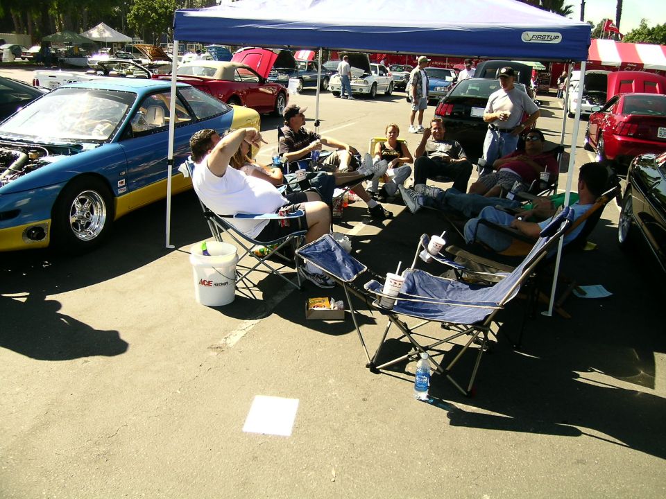 Blue and yellow 1993 Ford Probe with hood open, people sitting in chairs under a tent