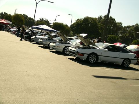1993 Ford Probe - A line of cars, including a white 1993 Ford Probe with its hood open, are parked at an outdoor event.