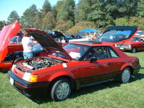 1978 Ford Mustang II - A red coupe with its hood and trunk open is displayed outdoors with other vehicles.