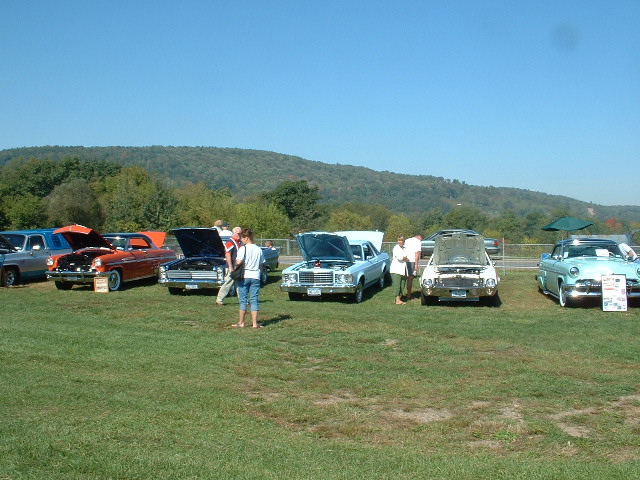 Light blue coupe with hood open, front view, at an outdoor car show