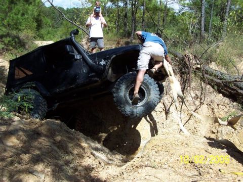 1987 Ford Bronco - A black Jeep Wrangler struggles on a sandy incline during an off-road excursion, with a person attempting to assist.