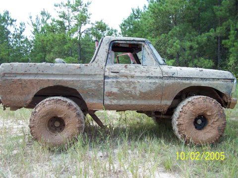1987 Ford Bronco - This heavily mud-caked vehicle sits in a field with trees in the background, showing off its off-road tires.