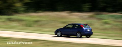 2002 Ford Focus - A blue 2002 Ford Focus is captured in motion on a paved road with a blurred background.