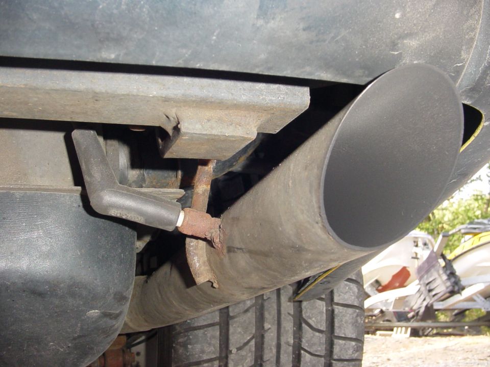 Exhaust pipe and tire of a vehicle, with a jet ski on a trailer in the background