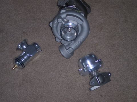 1999 Mitsubishi Mirage - A turbocharger and two related components, possibly for a performance upgrade, are laid out on a carpeted surface.