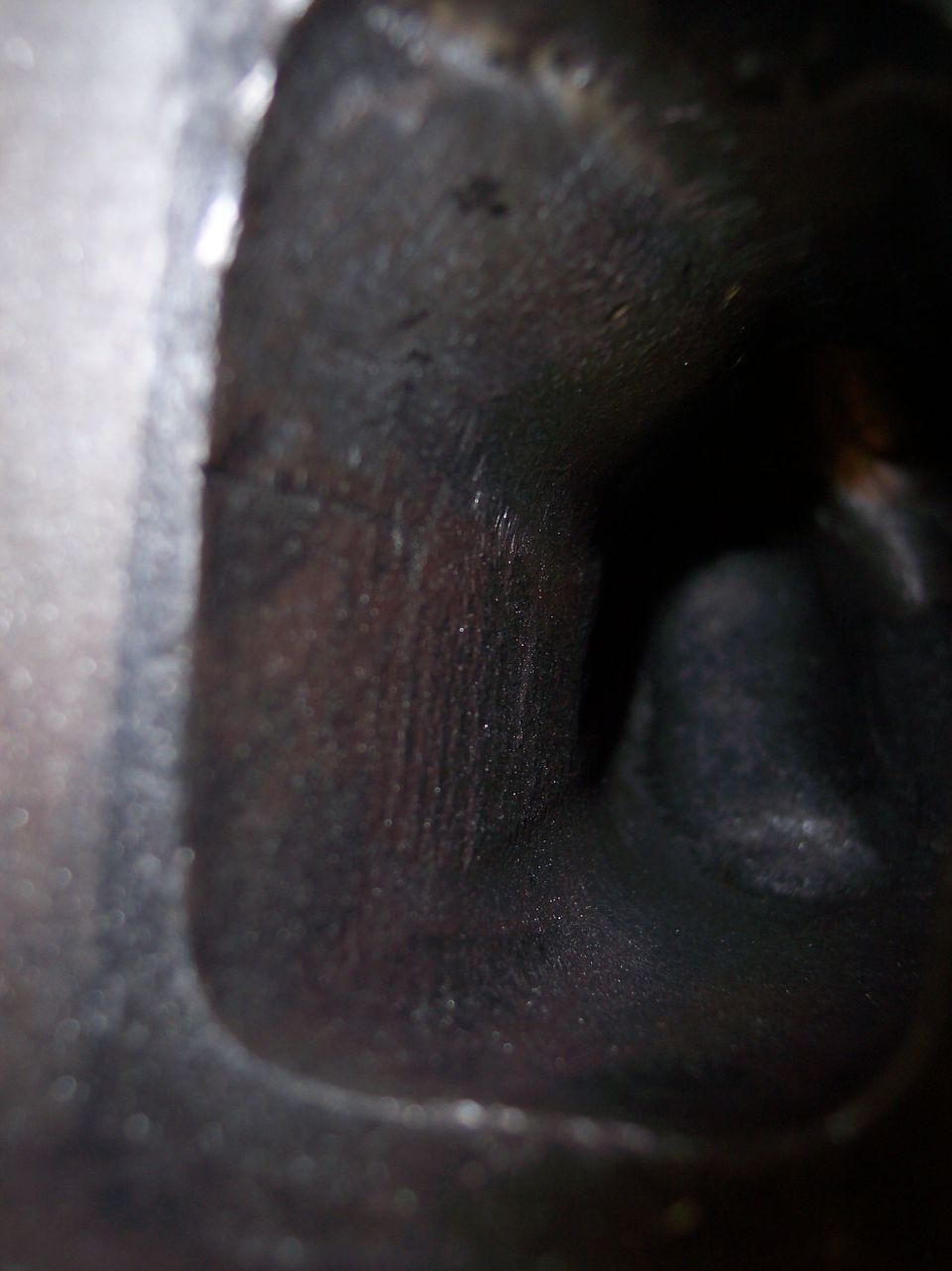 Close-up of a dark, internal engine component, possibly a cylinder head, showing machined surfaces and some carbon buildup