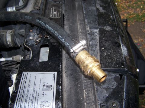 1996 Ford Bronco - A black hose with a brass quick disconnect fitting is attached to a metal bracket in the engine bay.