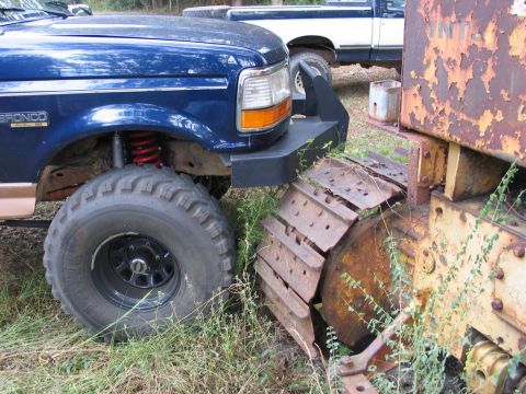 1995 Ford Bronco - A blue 1995 Ford Bronco is parked next to a rusty bulldozer, with another truck visible in the background.