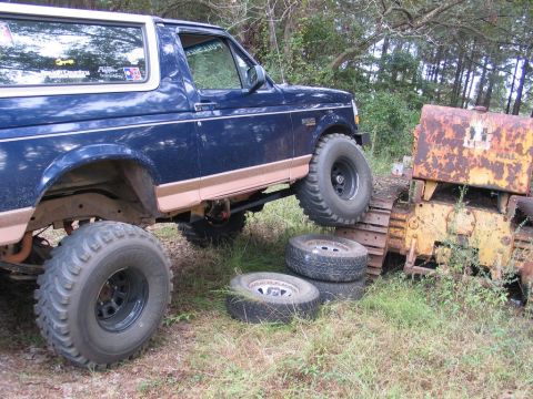 1995 Ford Bronco - Modified 1995 Ford Bronco navigates over a rusty bulldozer in an outdoor scene.