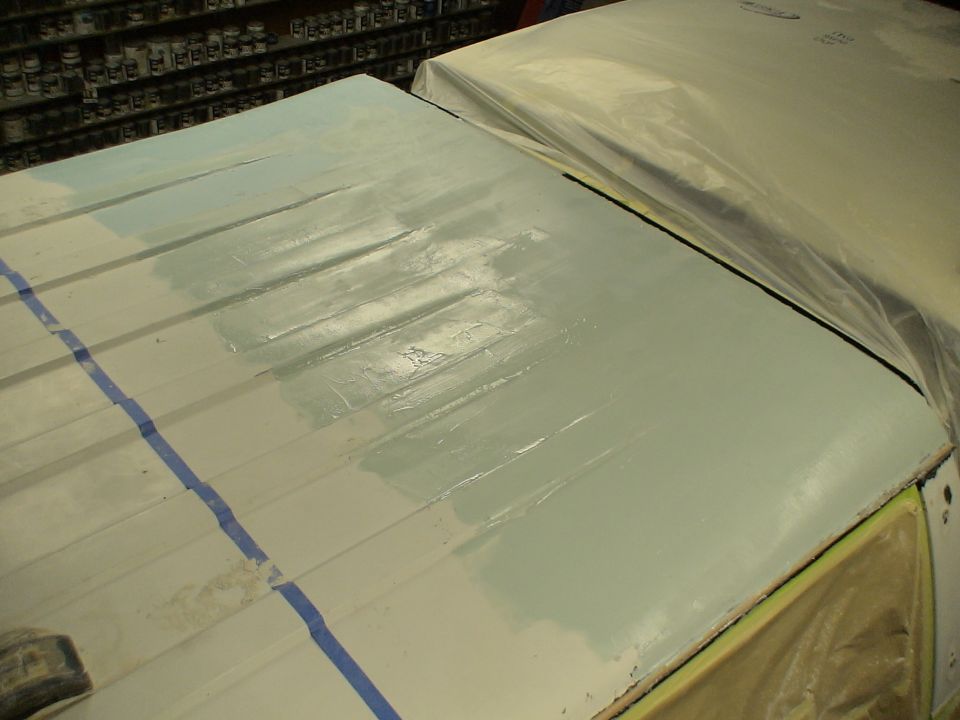 Hood or roof panel in shop with primer and filler being block-sanded, blue tape lines