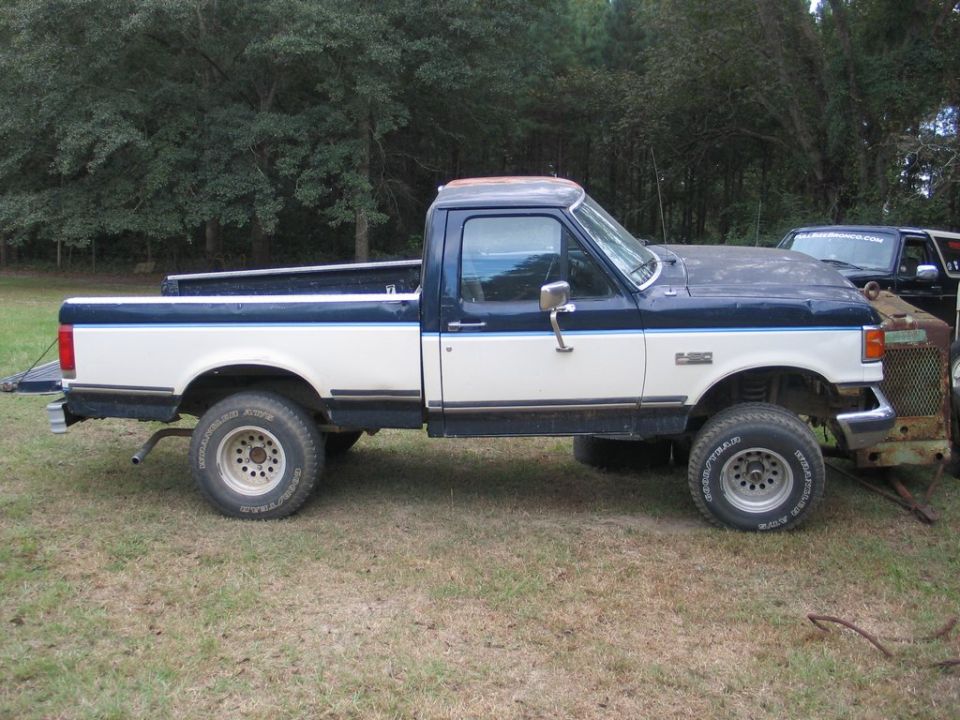 Two-tone blue and white Ford F-150 pickup truck, lifted, with aftermarket wheels