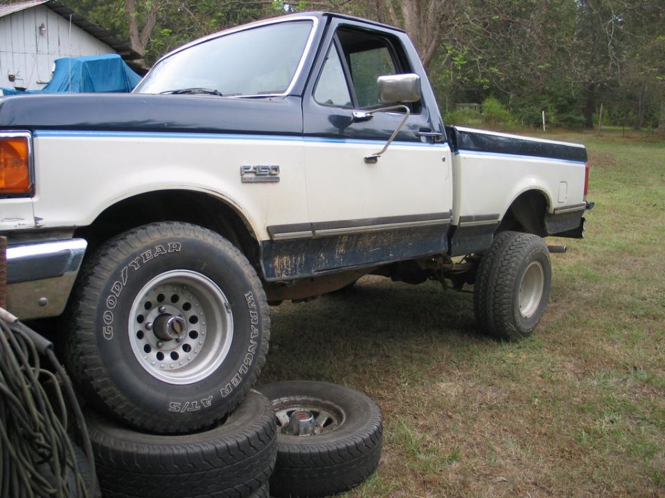 1989 Ford F-150 pickup truck, white and blue two-tone paint, parked outdoors with spare tires nearby