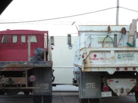 1992 Ford Bronco - Two work trucks are seen from the rear, one red and one white, with various tools and equipment in their beds.