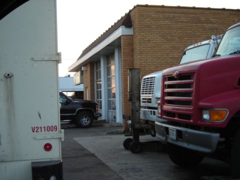 1992 Ford Bronco - Multiple trucks are parked in front of a commercial building. The white truck has 'V211009' on its side.