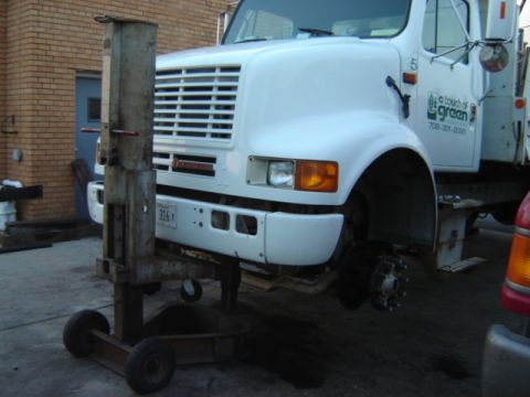 1992 Ford Bronco - A white truck is being serviced, with its front wheel removed and the vehicle elevated by a lift.