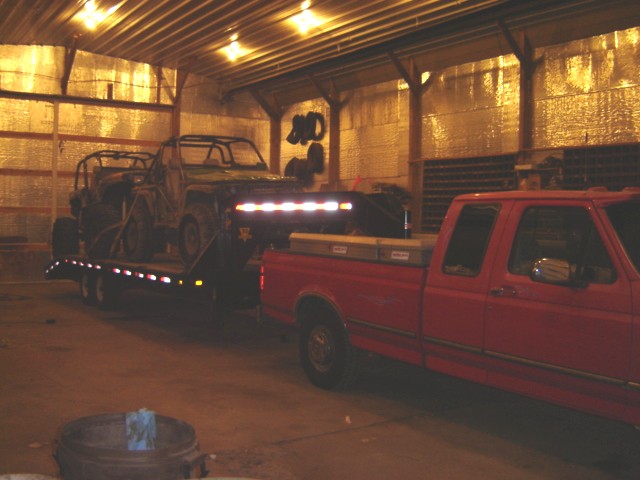 Red pickup truck towing a trailer with two ATVs inside a garage