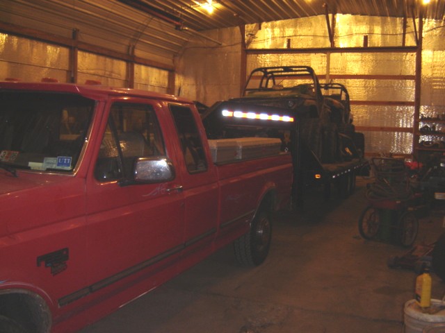 red pickup truck parked next to a trailer carrying a vehicle with bright lights