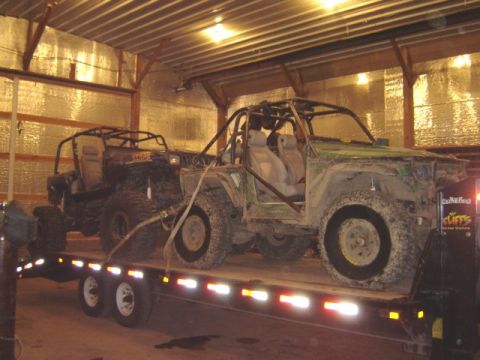 1992 Ford Bronco - Two modified off-road vehicles are transported on a trailer within a metal-clad structure.