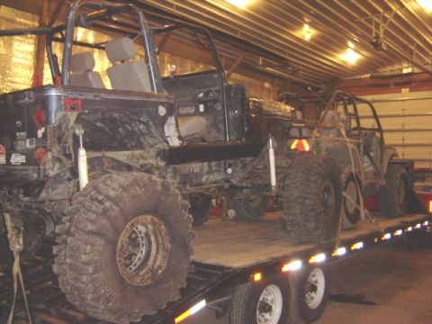 1992 Ford Bronco - Two custom off-road vehicles are loaded onto a flatbed trailer inside a garage.