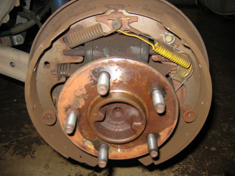 Close-up of a rusty drum brake assembly with brake shoes, springs, and wheel studs
