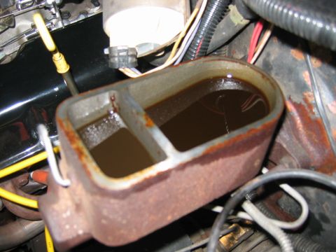 1985 Ford LTD Crown Victoria - Close-up of a rusty brake master cylinder filled with dark fluid, showing engine components in the background.