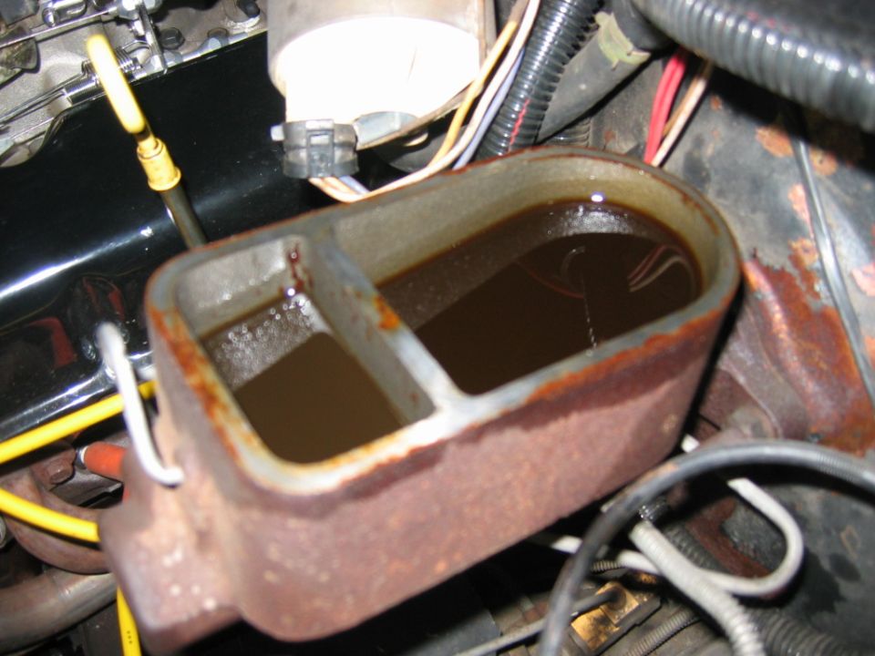 rusty brake master cylinder with dark fluid inside, engine components visible