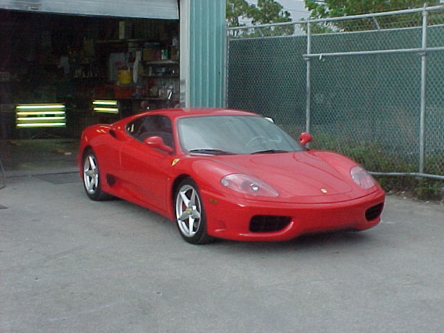 Red sports car parked on concrete in front of a garage and chain-link fence