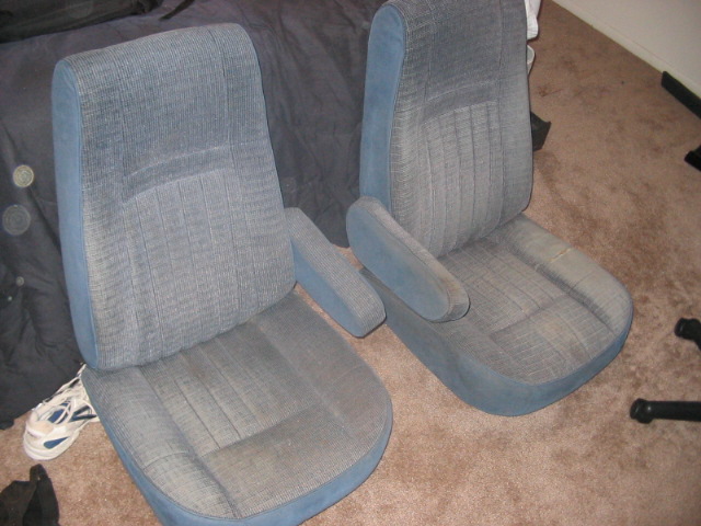 Two blue fabric car seats with armrests sit on a carpeted floor