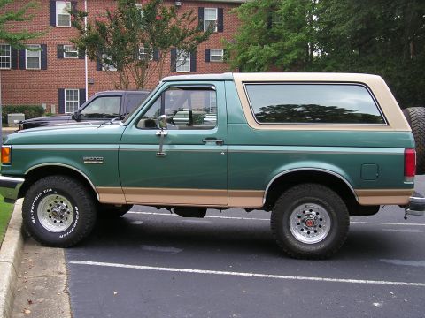 1989 Ford Bronco - Side view of a green and tan Ford Bronco with aftermarket wheels and tires.
