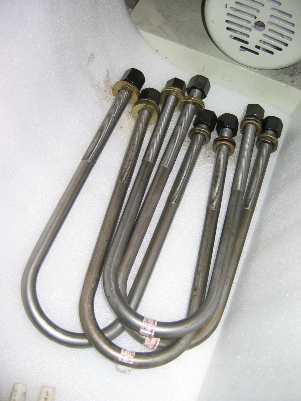 Set of metal U-bolts with nuts and washers laid out on foam packing surface
