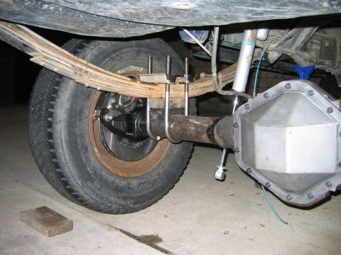 1985 Ford Bronco - Close-up of a vehicle's rear axle assembly, leaf springs, a custom differential cover, and a shock absorber.