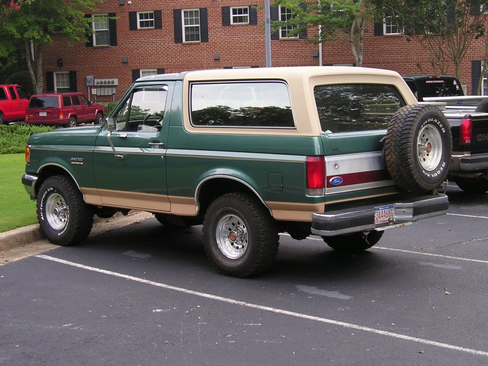Green and tan Ford Bronco, rear three-quarter view in a parking lot with rear spare tire