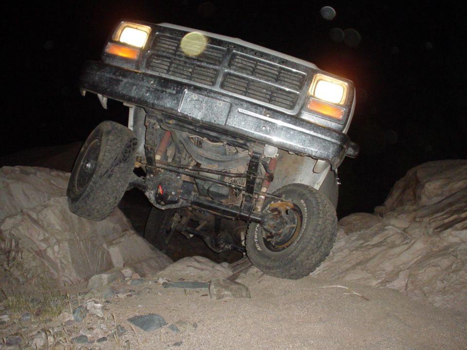 Front end of lifted truck at night, hood removed, front wheels straddling rocks