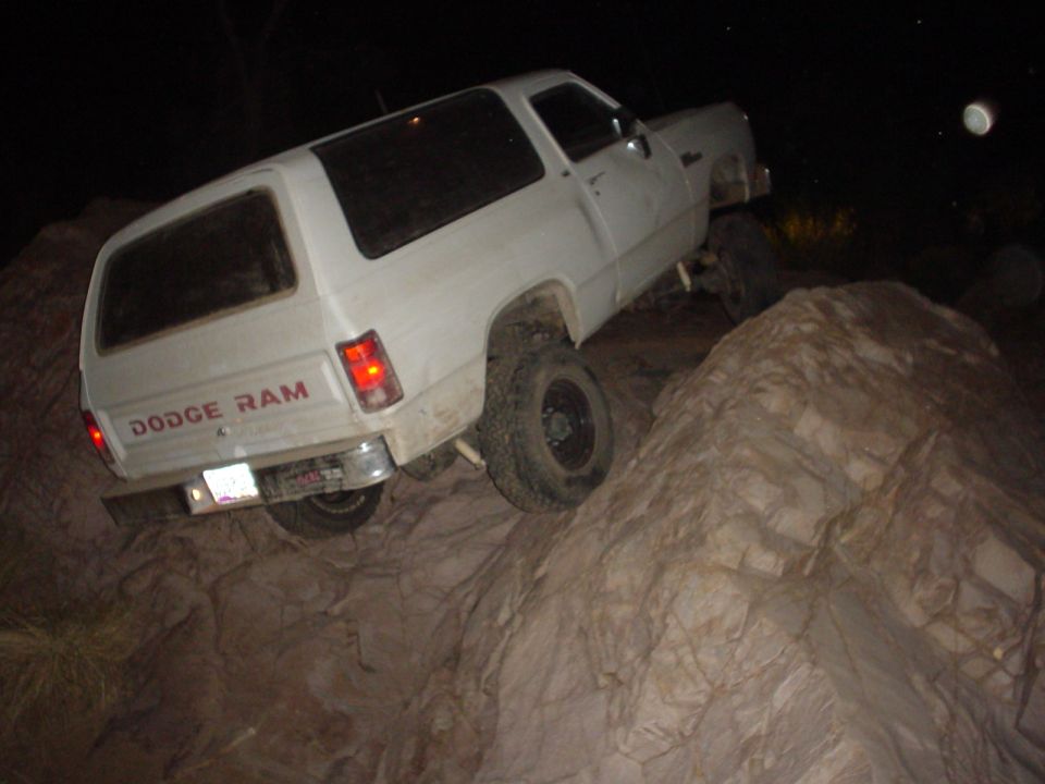 White Dodge Ram SUV off-roading on rocks at night. The rear shows 'DODGE RAM' badging