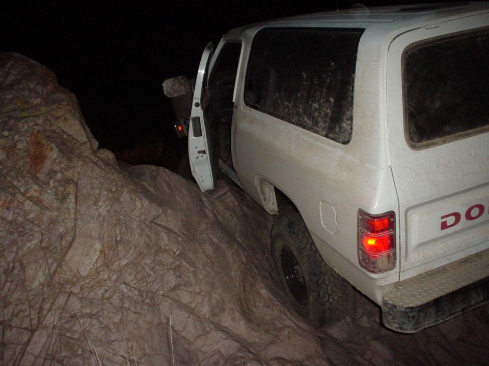 White Dodge Ramcharger with door open, stuck on a rocky incline at night