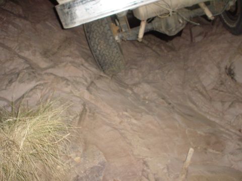 1981 Ford F-150 - The rear axle and tire of a truck are visible against a rocky, uneven surface.