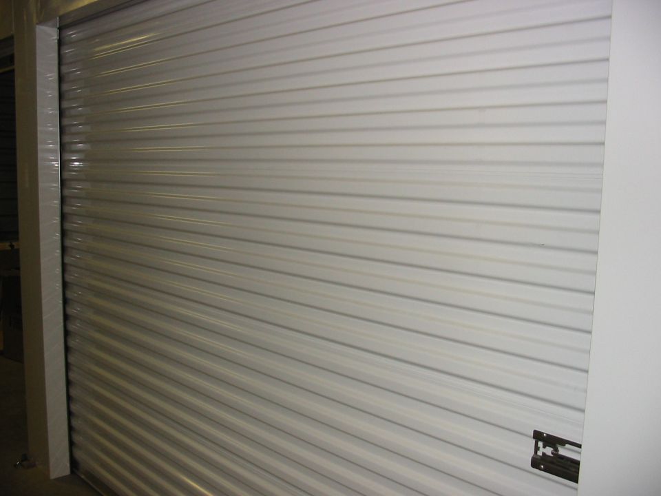 White corrugated metal garage door with a Supermotors.net logo in the lower right corner