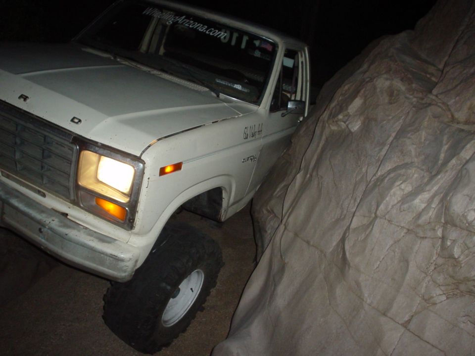 White 1981 Ford F-150 driving between rocks, with 'WheelingArizona.com' sticker on windshield