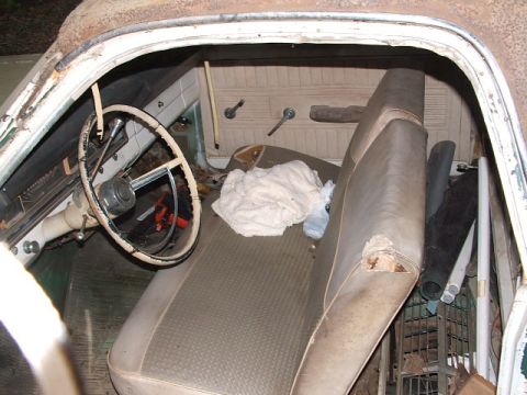 1966 Ford Ranchero - The interior of an old vehicle shows a worn bench seat, steering wheel, and door panels, with various items stored inside.