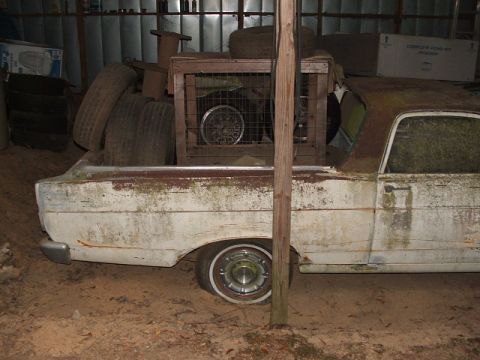 1966 Ford Ranchero - A weathered 1966 Ford Ranchero sits in storage, its bed filled with old tires and a spare wheel.