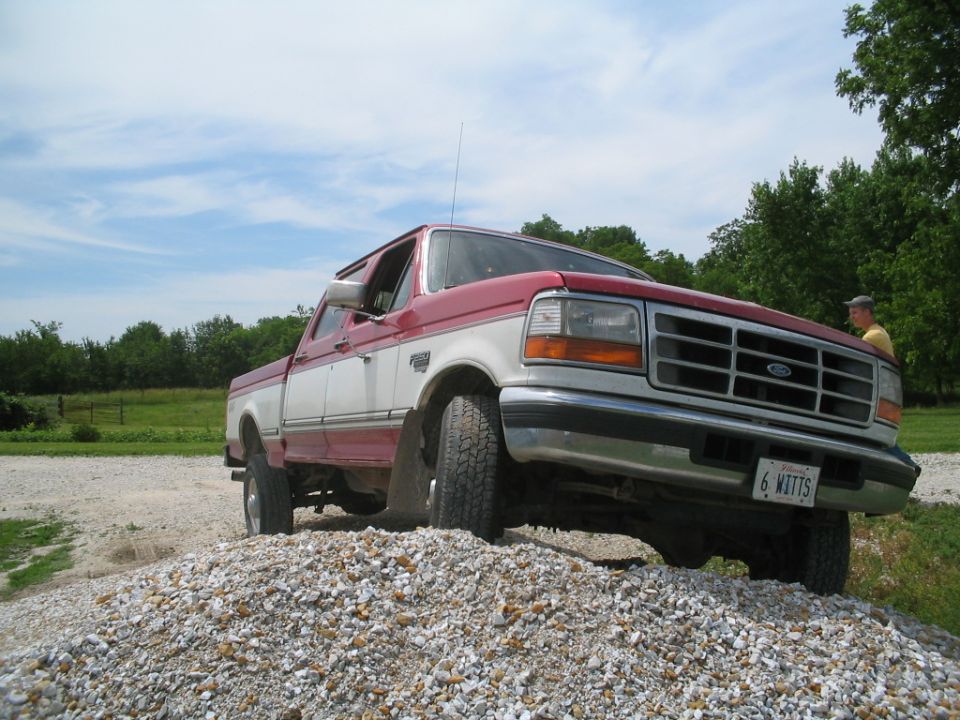 Red and white Ford pickup truck on a pile of gravel, with a man standing in the background