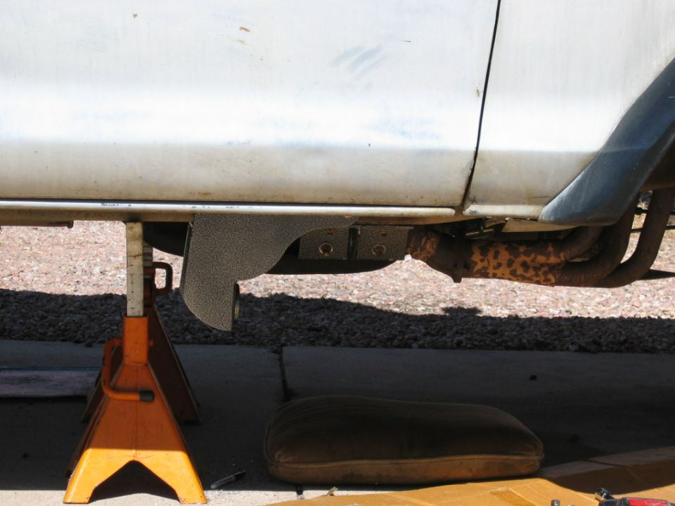 Silver vehicle underside on orange jack stand with rusty exhaust and body mount visible