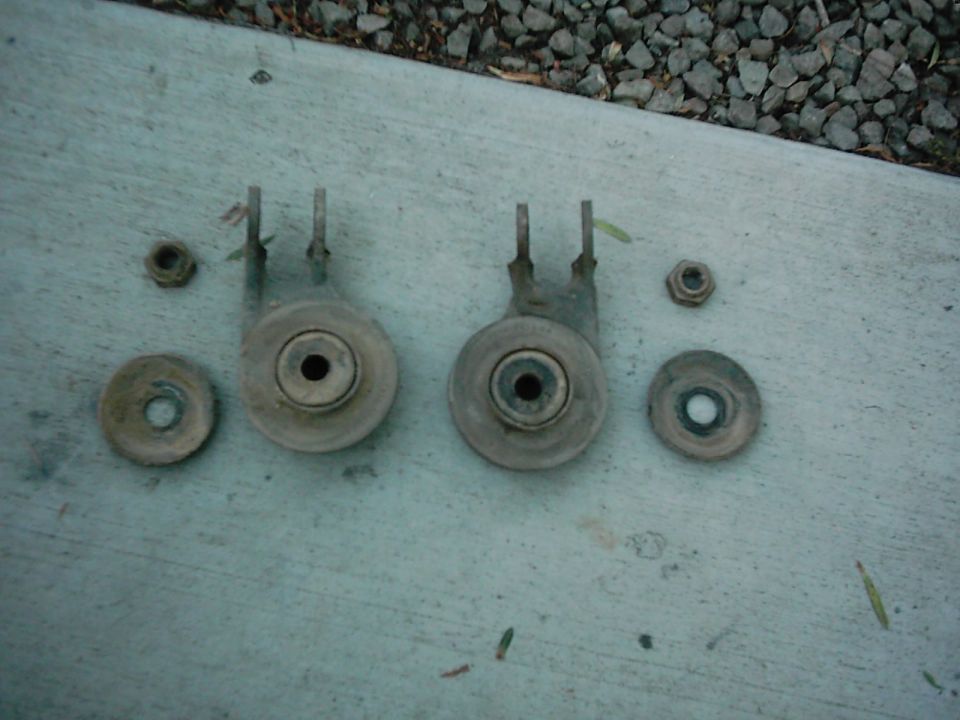 Two rusty suspension brackets with bolts and nuts on a concrete surface